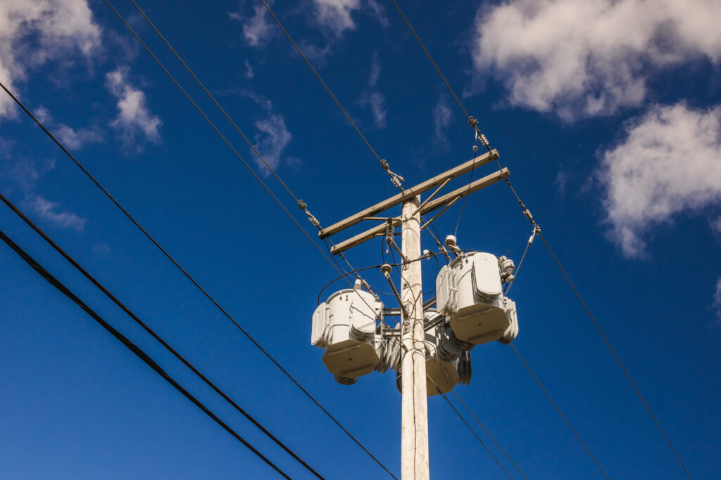 Utility pole with pole-mounted transformers and power lines against a blue sky