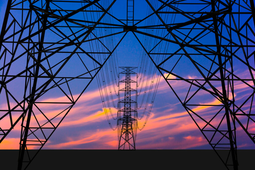 High-voltage transmission tower framing power lines against a sunset sky