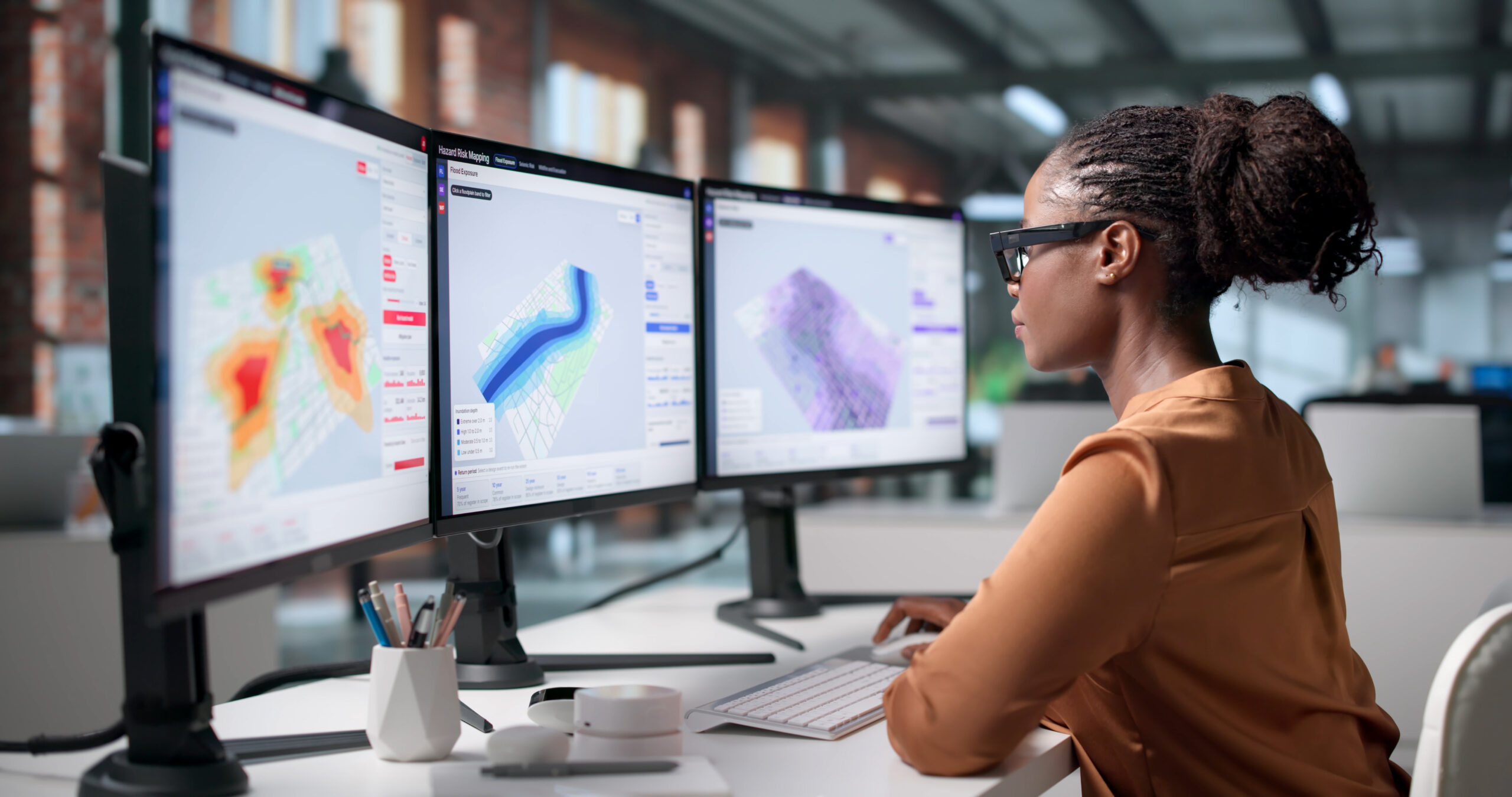 GIS analyst reviewing flood risk maps across three monitors