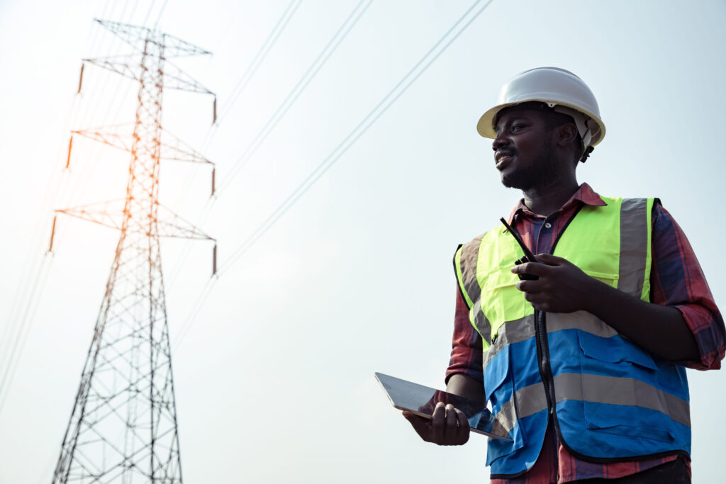 Field engineer with a tablet and radio beneath high-voltage transmission lines