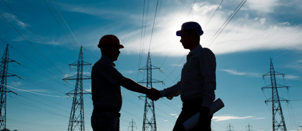 Silhouettes of two engineers shaking hands in front of transmission towers