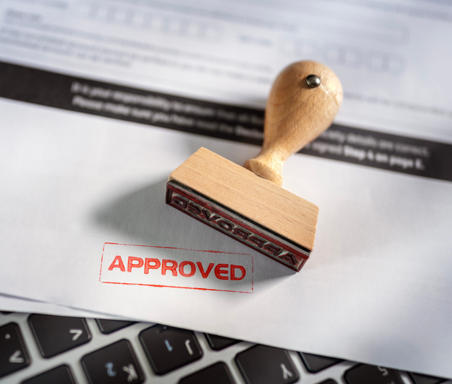 Rubber stamp marking a document Approved, resting on a laptop keyboard
