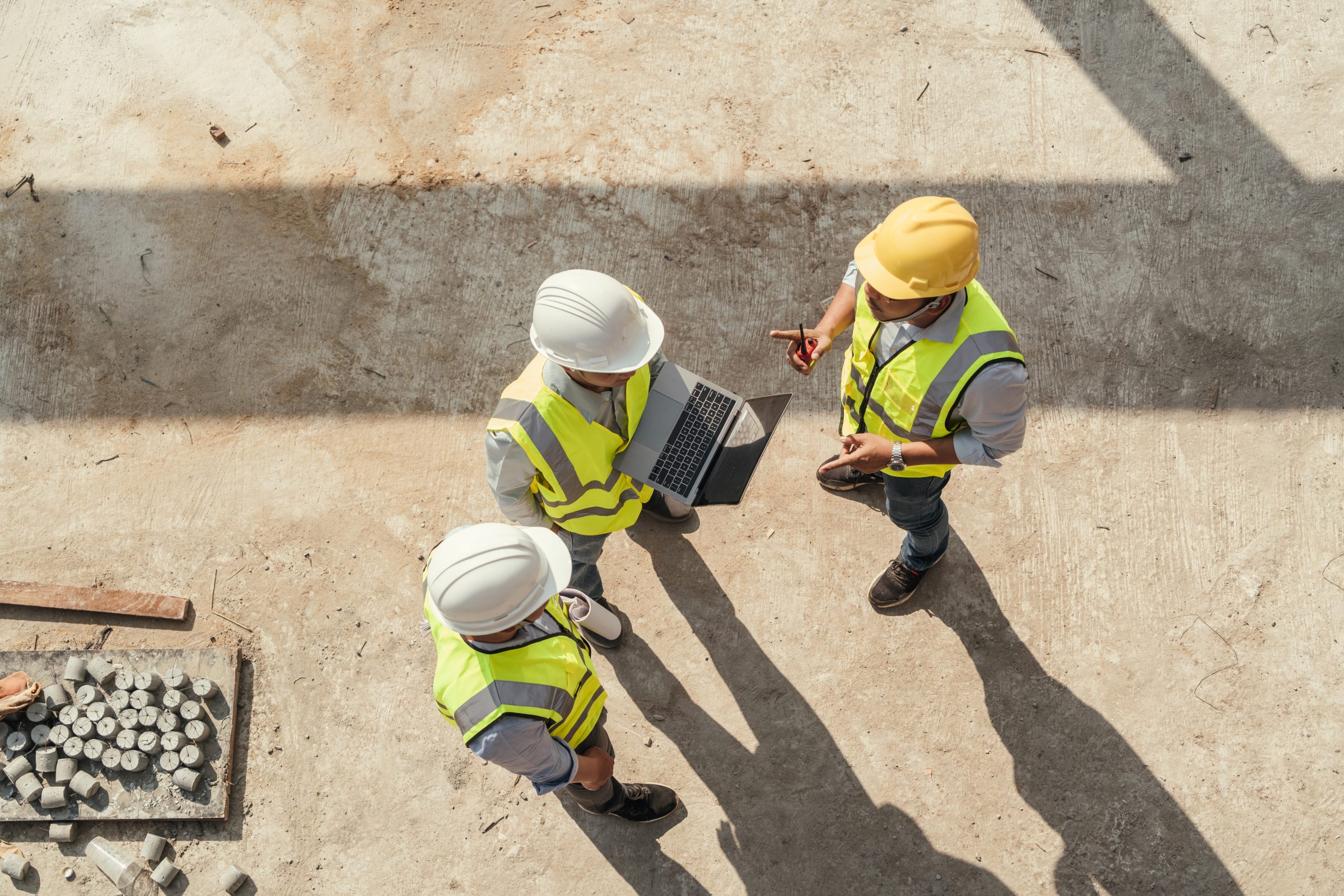 Overhead view of three engineers in hard hats reviewing a laptop on site