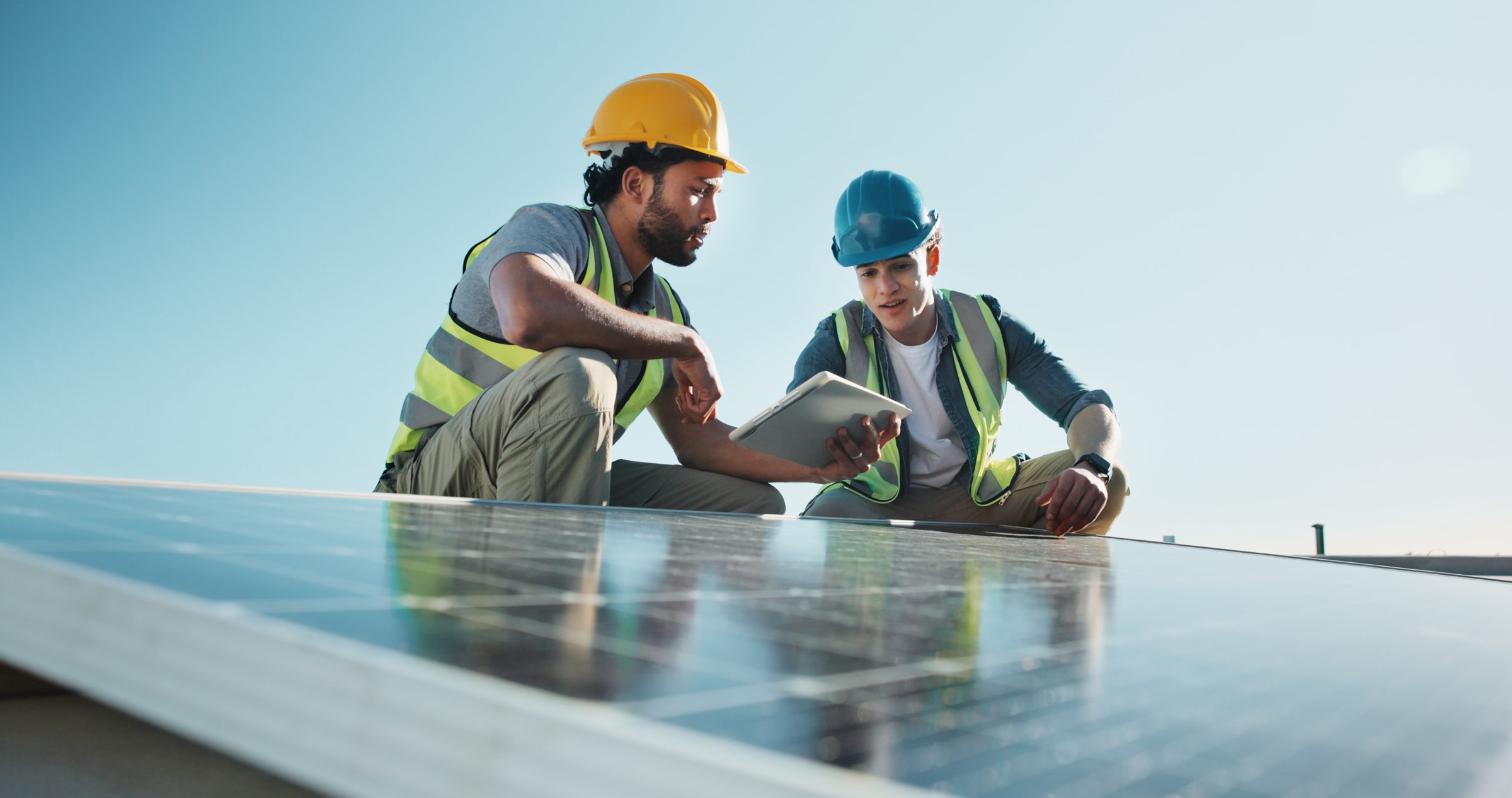 Engineers in hard hats reviewing a tablet beside solar panels